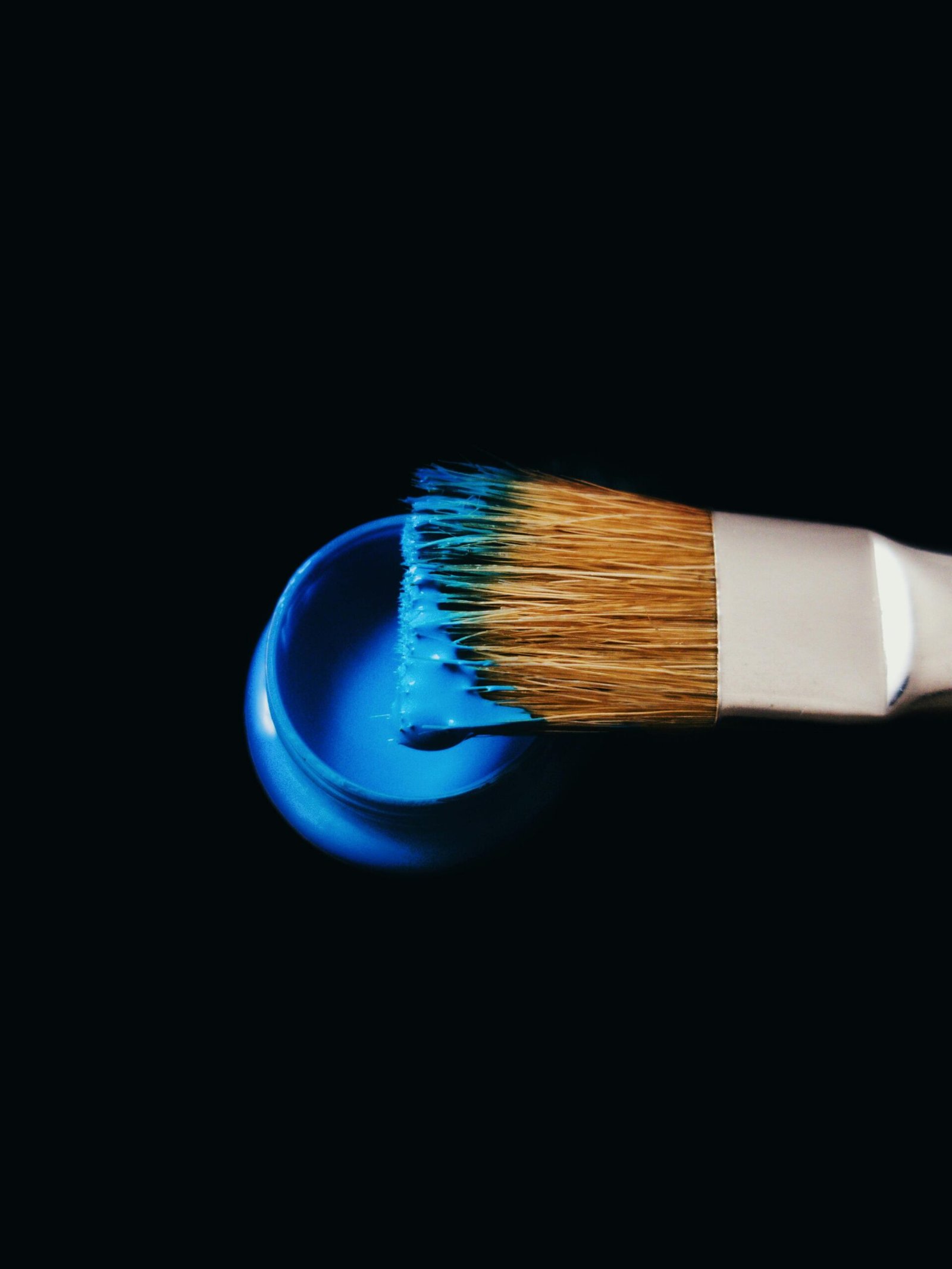 Close-up of paintbrush dipped in blue acrylic paint, emphasizing creativity.