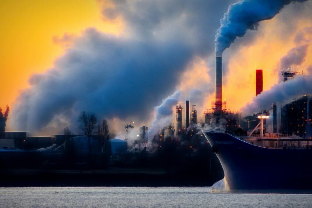 A factory emits thick smoke and pollution against a vibrant sunset, highlighting industrial impact on the environment.